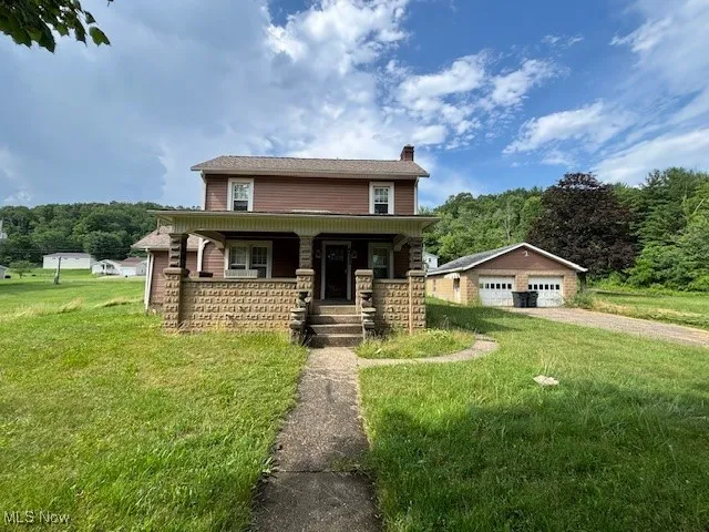 View of front of house featuring a detached garage, a chimney, a porch, an outdoor structure, and a front lawn