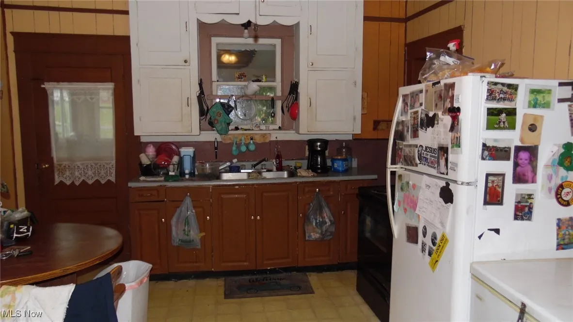 Kitchen with freestanding refrigerator, stove, light countertops, and brown cabinets