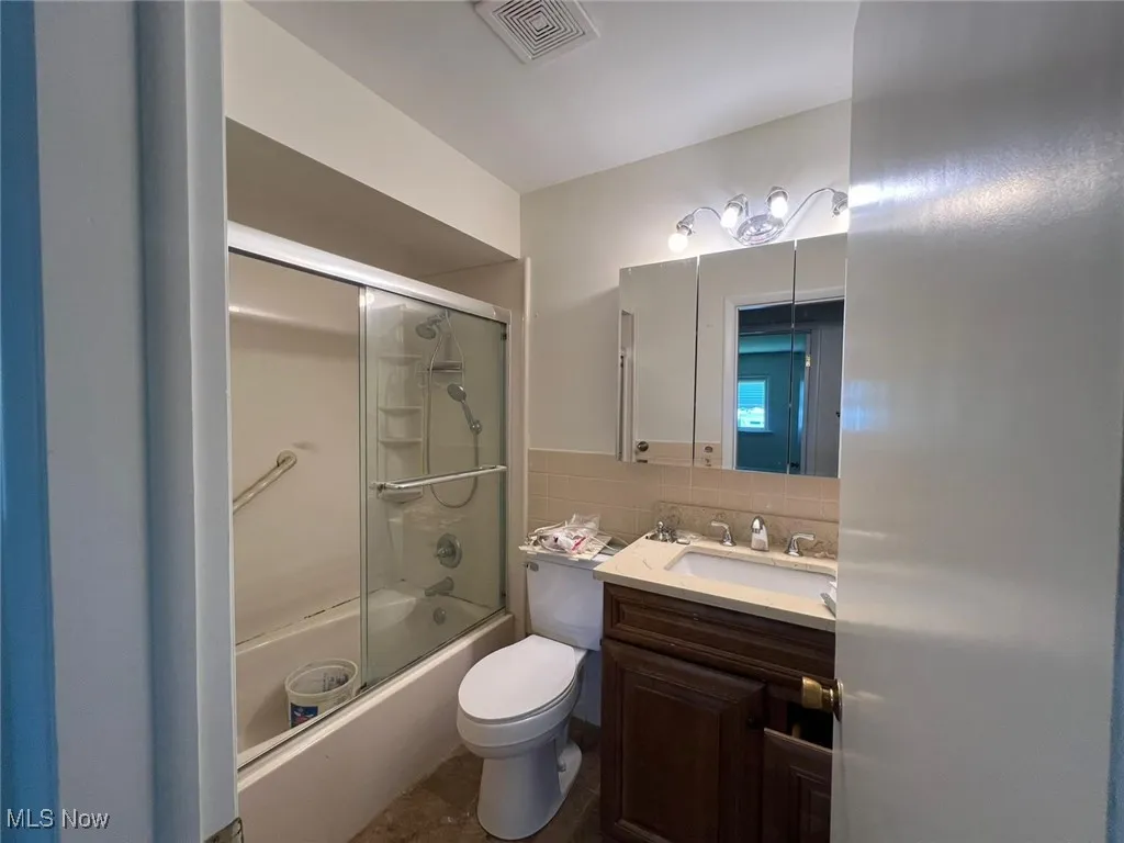Bathroom featuring vanity, enclosed tub / shower combo, tile walls, and tasteful backsplash