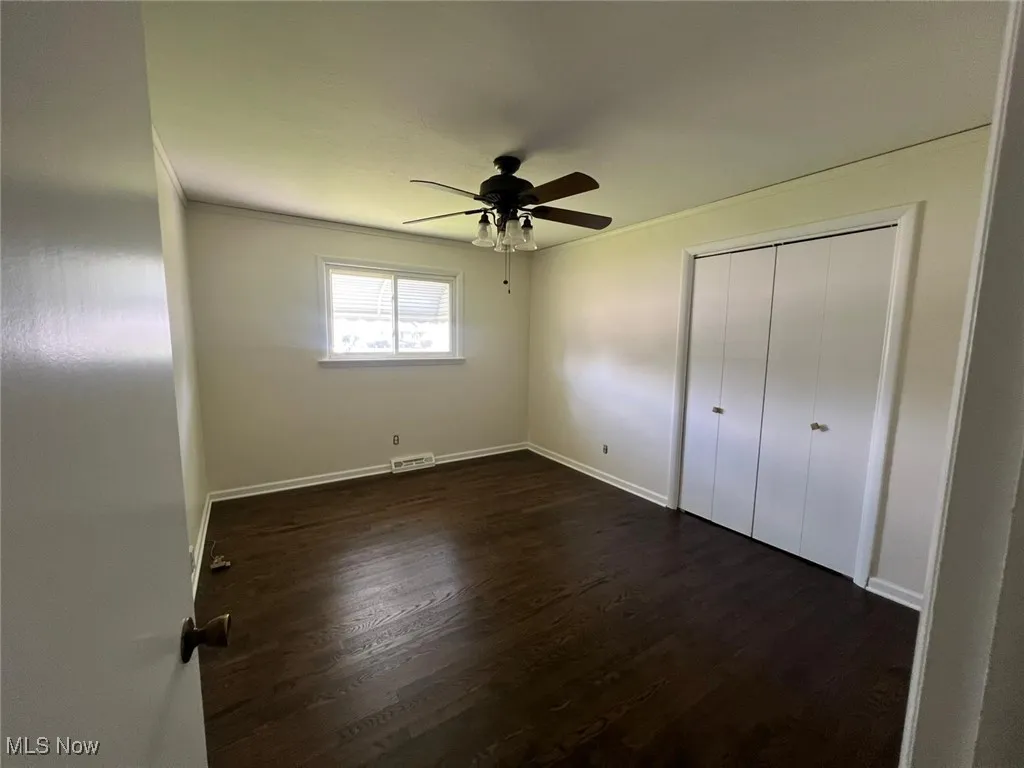 Unfurnished bedroom with dark wood finished floors, crown molding, a ceiling fan, and a closet