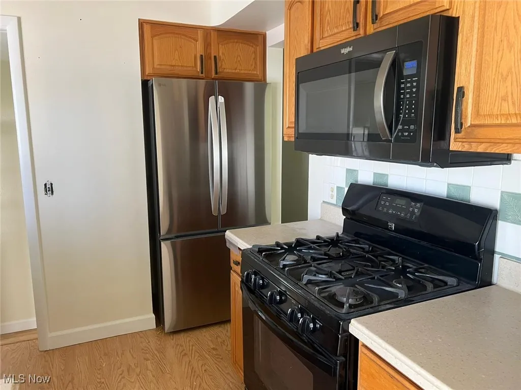 Kitchen featuring black appliances, light countertops, light wood-style flooring, and backsplash