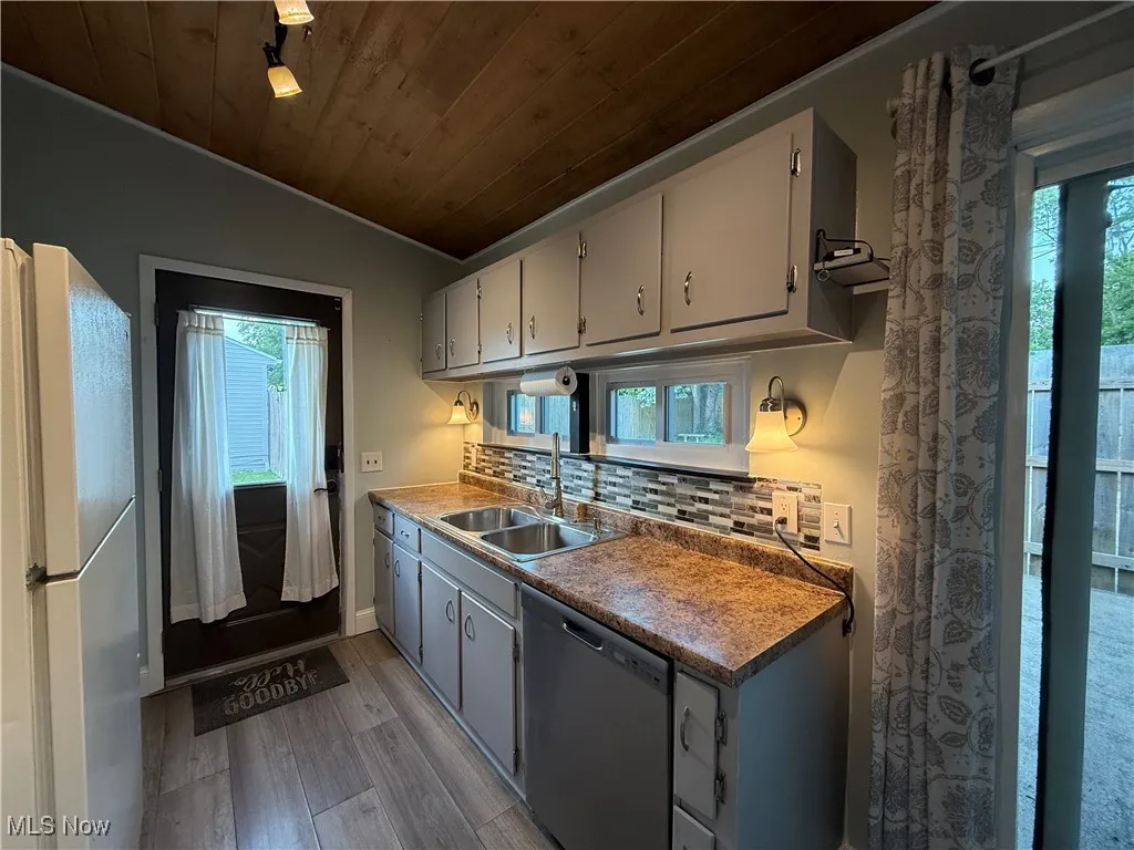 Kitchen with stainless steel dishwasher, wood finished floors, freestanding refrigerator, wood ceiling, and decorative backsplash