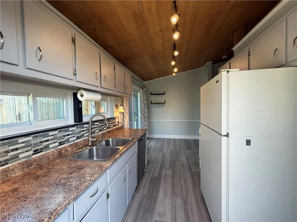 Kitchen with freestanding refrigerator, wood ceiling, decorative backsplash, dark wood-style floors, and stainless steel dishwasher