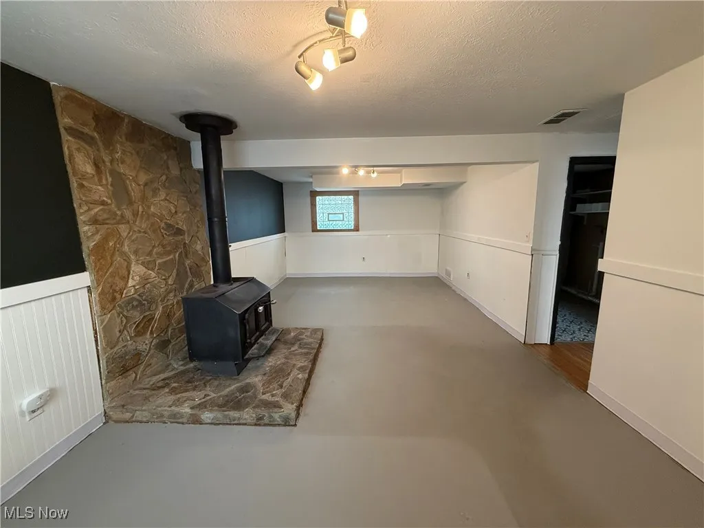 Below grade area with a wood stove, wainscoting, a textured ceiling, and track lighting
