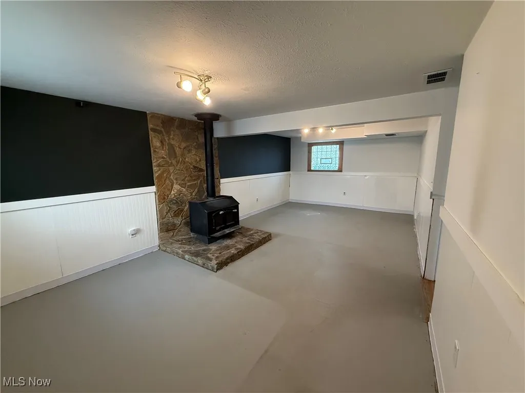 Unfurnished living room featuring a wainscoted wall, a wood stove, concrete floors, and a textured ceiling
