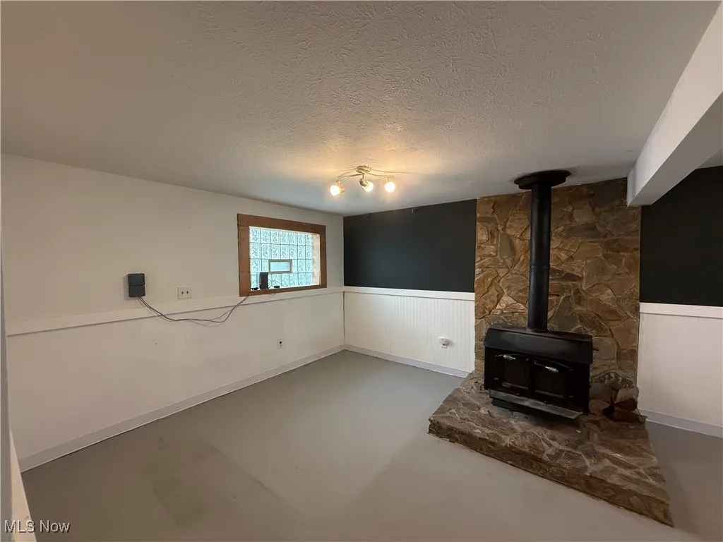 Unfurnished living room with a wainscoted wall, a wood stove, a textured ceiling, and concrete floors