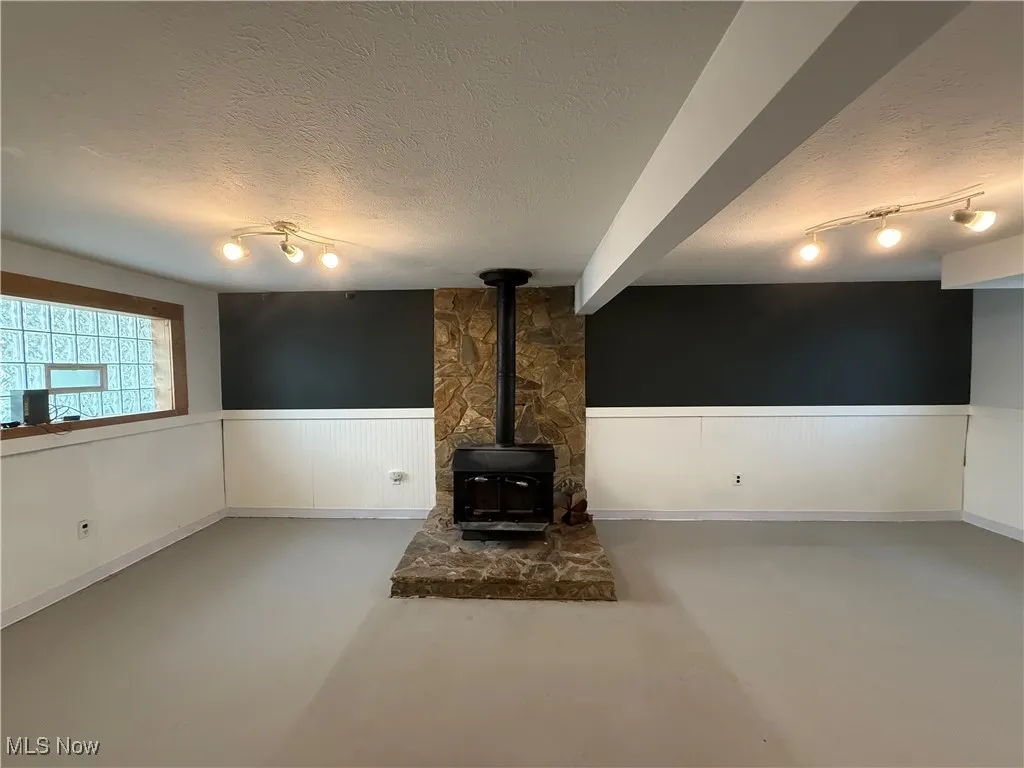 Unfurnished living room featuring a textured ceiling, a wood stove, wainscoting, and finished concrete floors