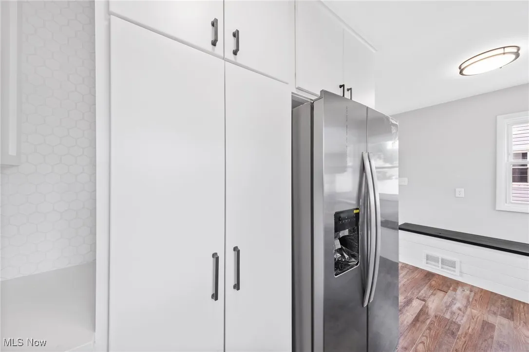 Kitchen with stainless steel fridge with ice dispenser, white cabinets, and wood finished floors