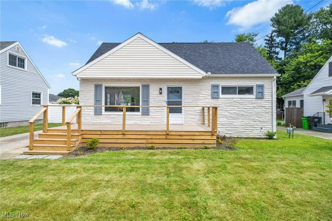 View of front of property featuring a wooden deck, a shingled roof, and a front yard