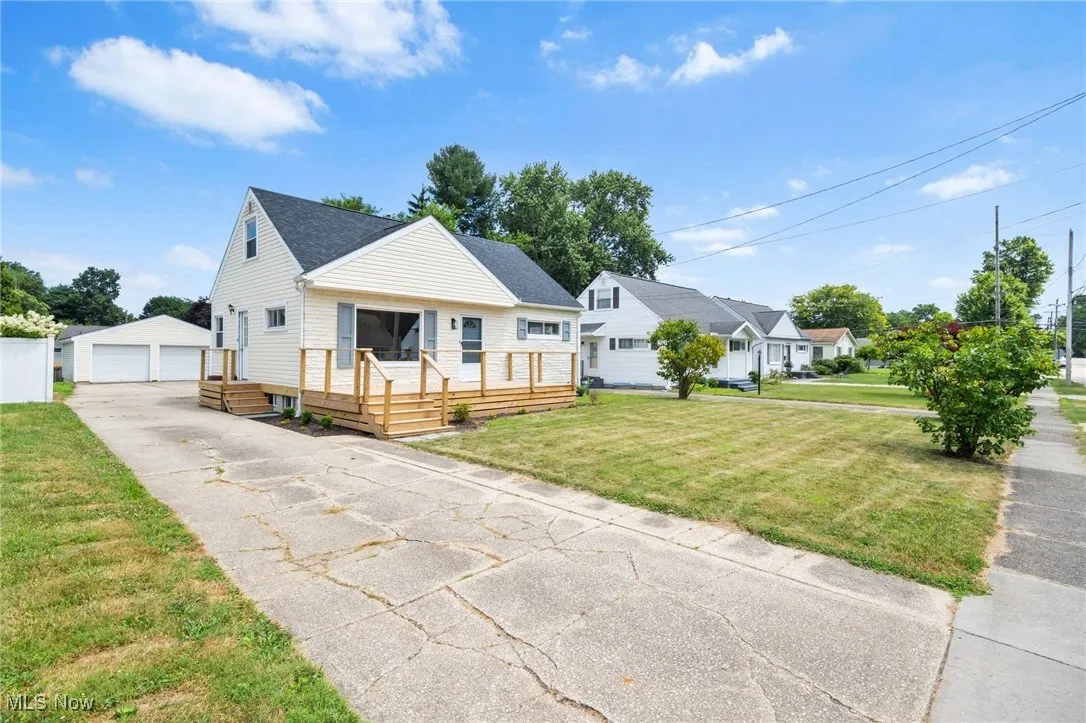 Bungalow-style house with an outdoor structure, a detached garage, a front lawn, roof with shingles, and a wooden deck