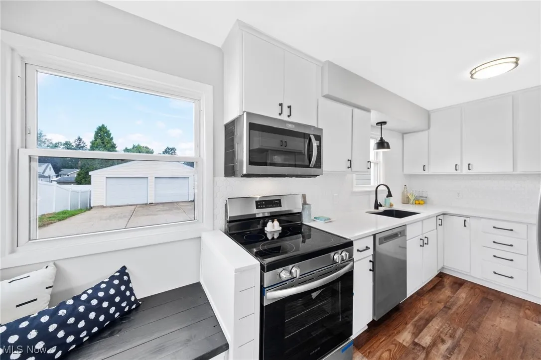 Kitchen featuring appliances with stainless steel finishes, dark wood-style floors, white cabinets, and tasteful backsplash