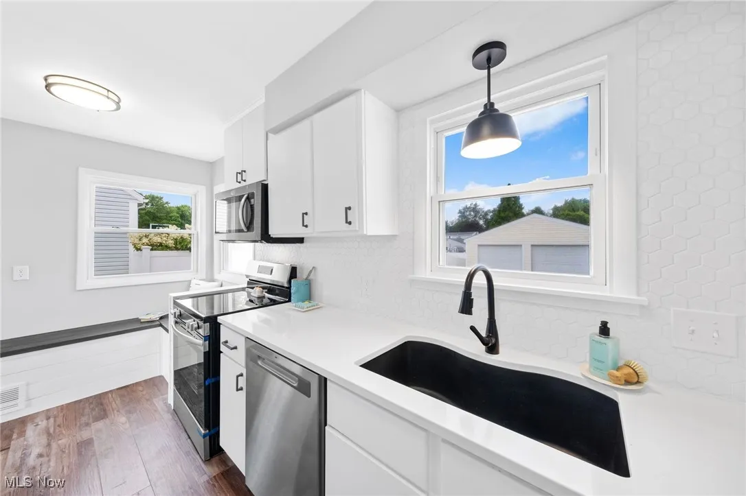 Kitchen featuring appliances with stainless steel finishes, decorative backsplash, light countertops, white cabinets, and pendant lighting