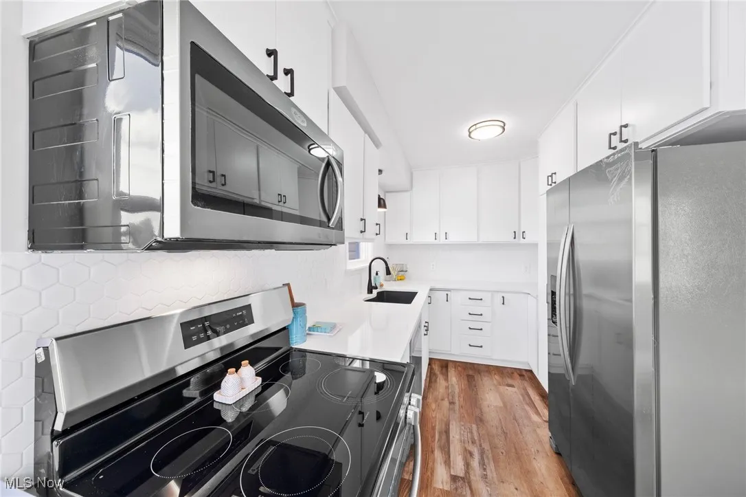 Kitchen with appliances with stainless steel finishes, wood finished floors, light countertops, white cabinetry, and backsplash