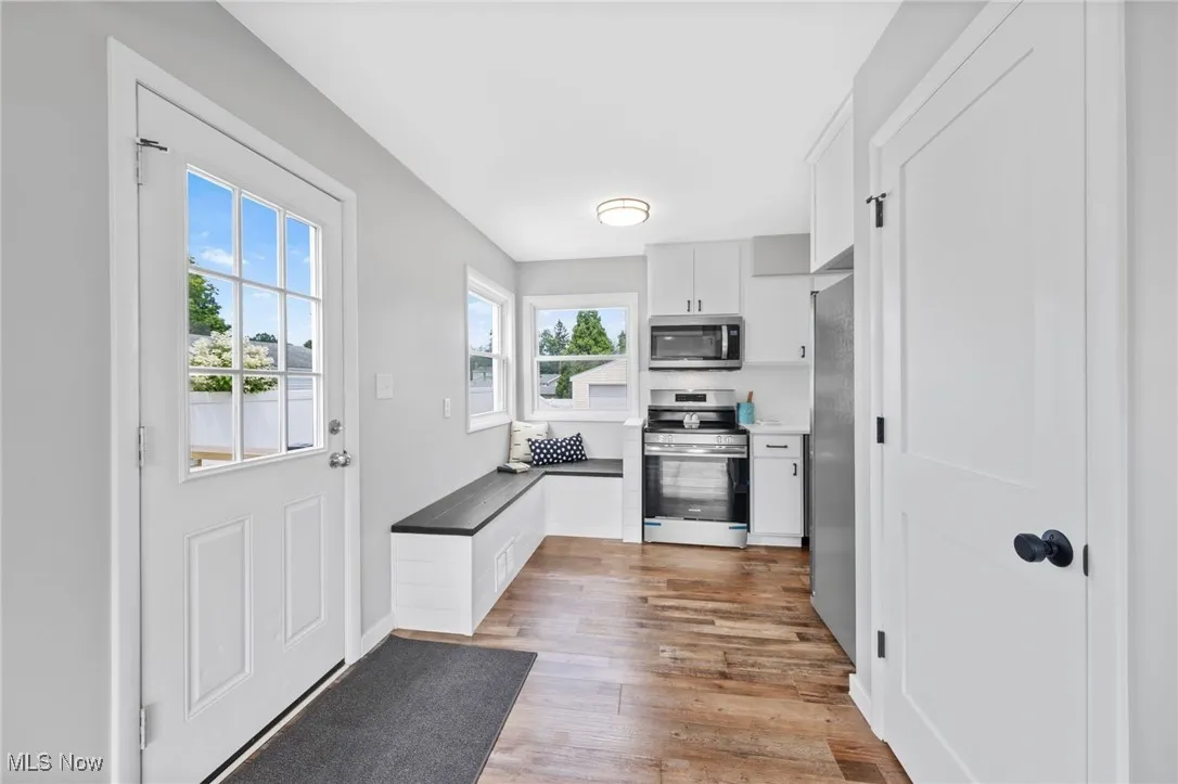 Kitchen featuring stainless steel appliances, white cabinets, wood finished floors, and dark countertops
