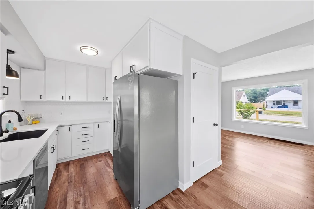Kitchen with appliances with stainless steel finishes, wood finished floors, white cabinetry, and light countertops