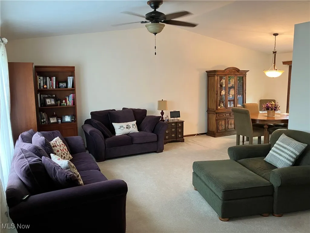 Living area with light colored carpet, vaulted ceiling, and a ceiling fan