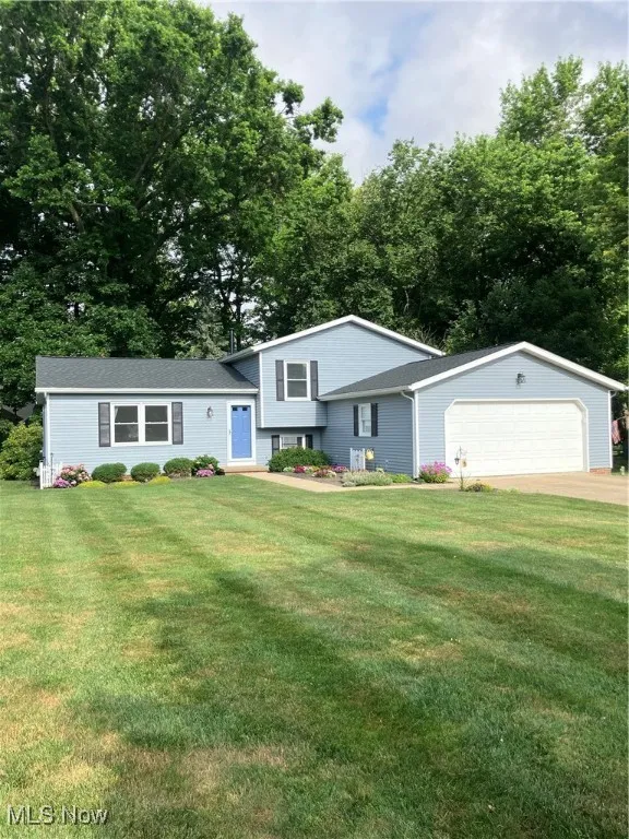 Tri-level home with a front yard, driveway, a shingled roof, and a garage