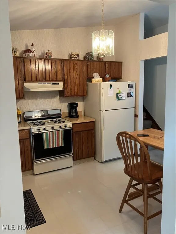 Kitchen featuring stove, refrigerator, extractor fan, a chandelier, and light countertops
