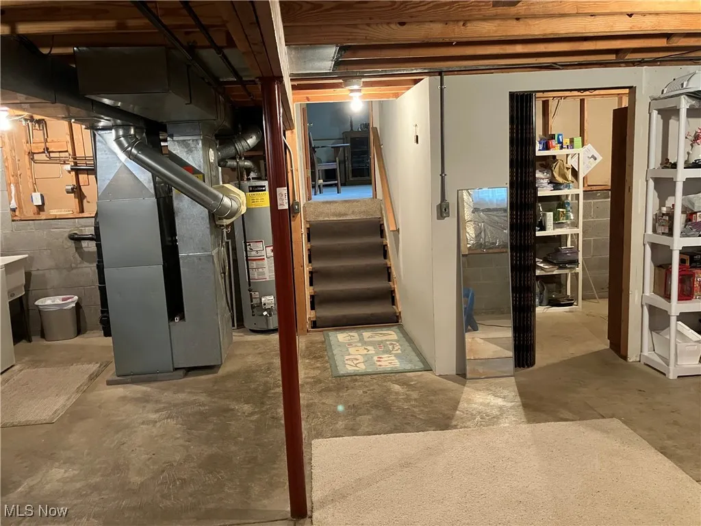 Unfinished basement with heating unit, stairs, and gas water heater