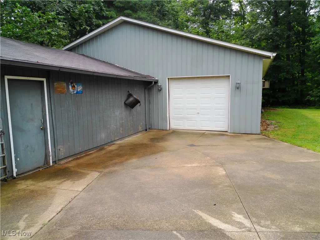 Detached garage featuring concrete driveway and view of scattered trees