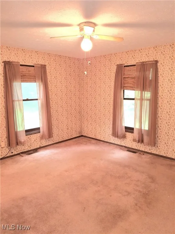 Unfurnished room featuring a textured ceiling, carpet floors, ceiling fan, and wallpapered walls