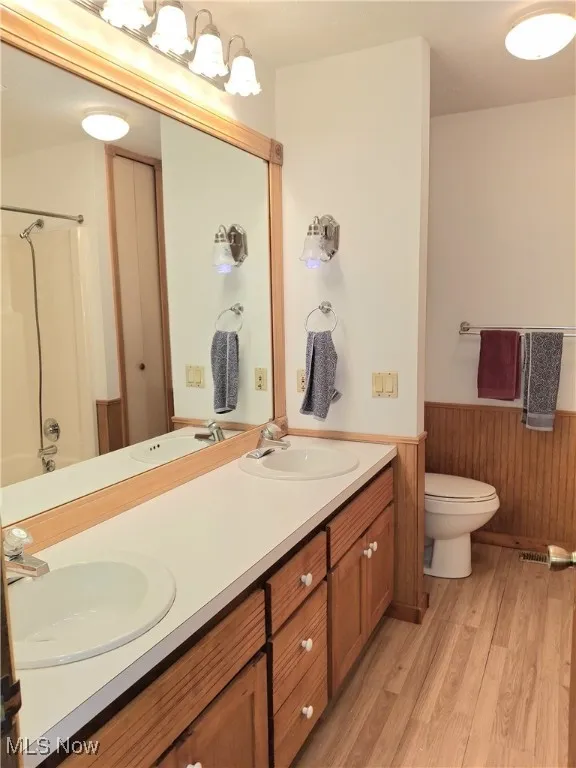 Full bath featuring wainscoting, double vanity, shower / bath combination, light wood-type flooring, and wooden walls