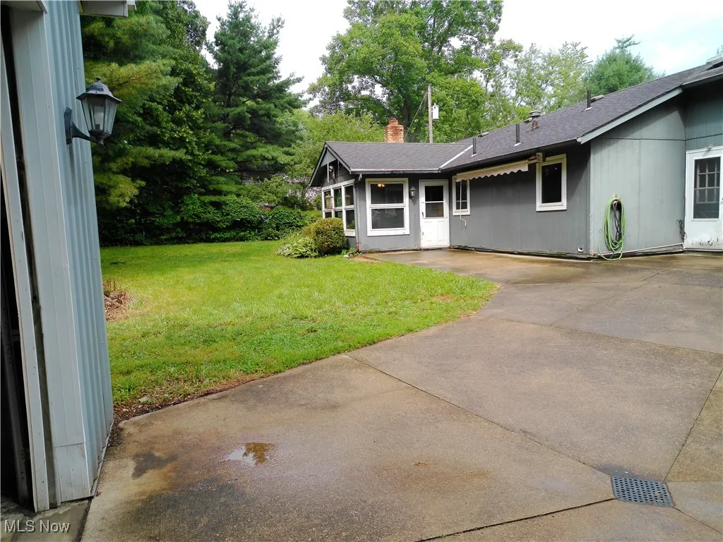 View of green lawn with driveway and a patio area