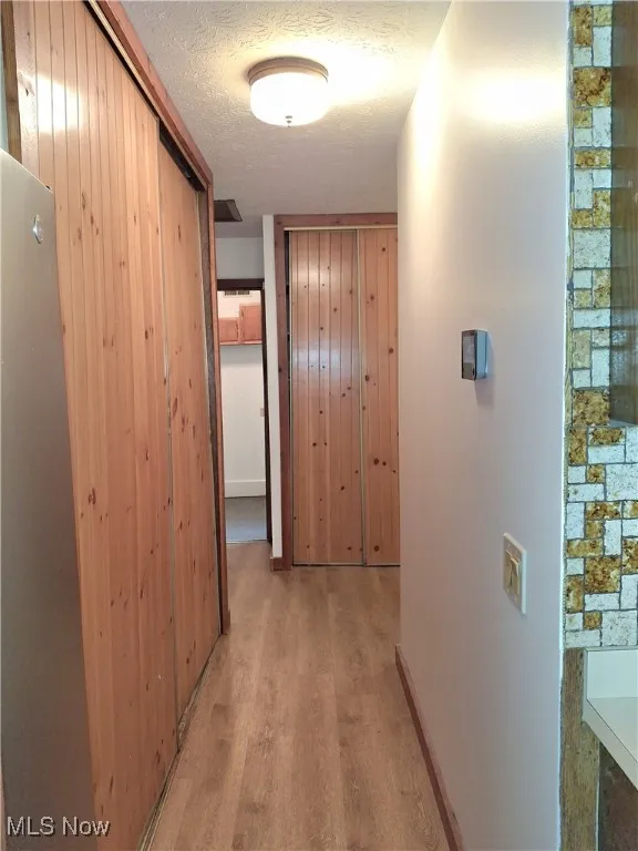Hall with a textured ceiling, light wood-style flooring, and wooden walls