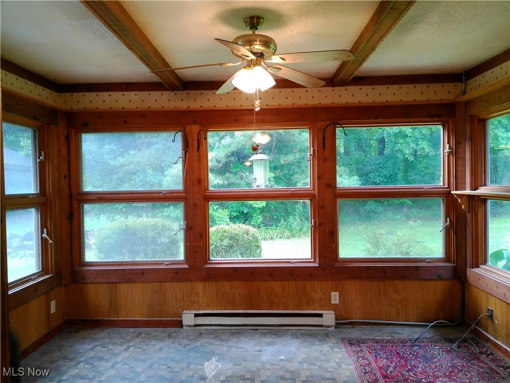 Unfurnished sunroom featuring a baseboard radiator, wooden walls, and beamed ceiling