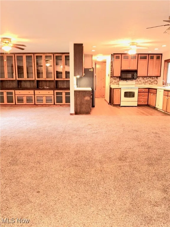 Kitchen with ceiling fan, white appliances, glass insert cabinets, decorative backsplash, and light countertops