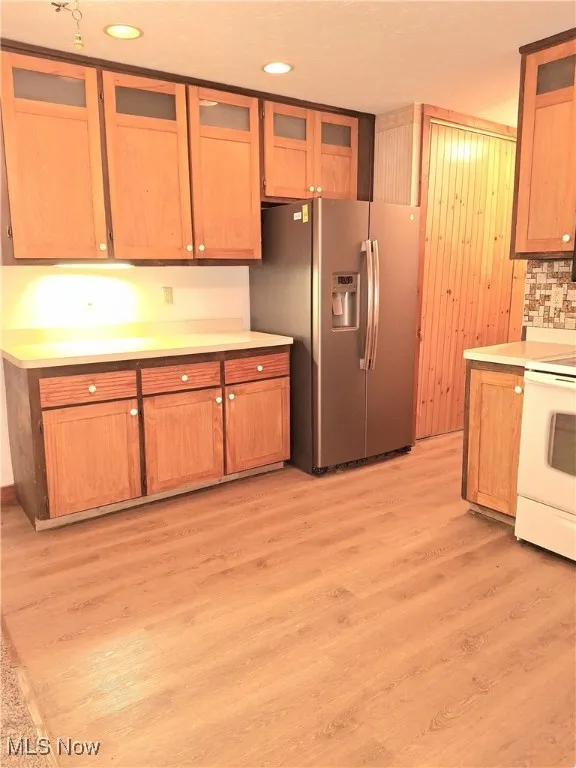 Kitchen featuring glass insert cabinets, light countertops, stainless steel fridge with ice dispenser, white range with electric stovetop, and recessed lighting