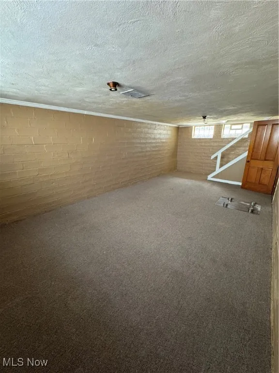 Carpeted empty room with brick wall and a textured ceiling