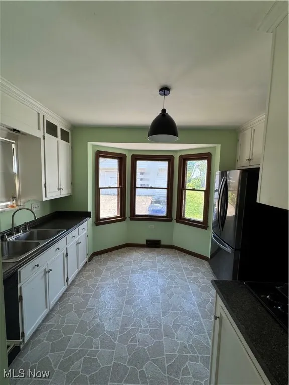 Kitchen featuring healthy amount of natural light, dark countertops, white cabinetry, and refrigerator