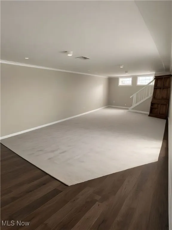 This picture is AI STAGED of basement area for imaginary purposes. Below grade area featuring ornamental molding and dark wood-style floors