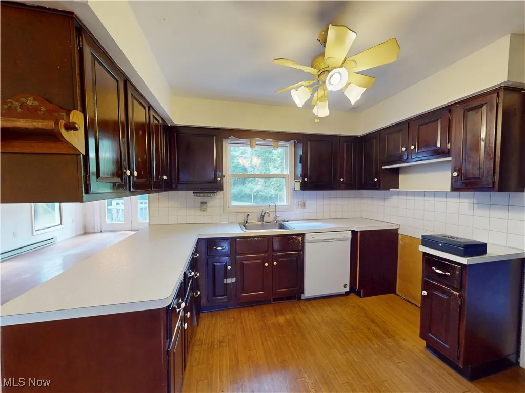 Kitchen with white dishwasher, light wood-type flooring, ceiling fan, decorative backsplash, and light countertops