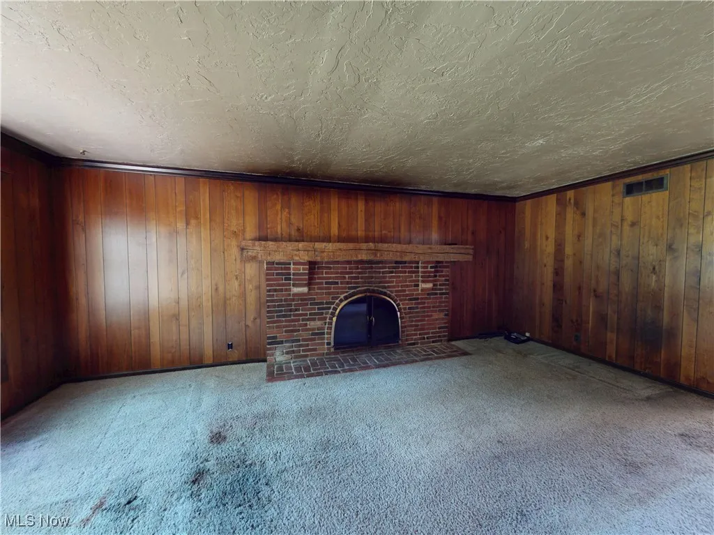 Unfurnished living room featuring a textured ceiling, a fireplace, carpet flooring, and wood walls