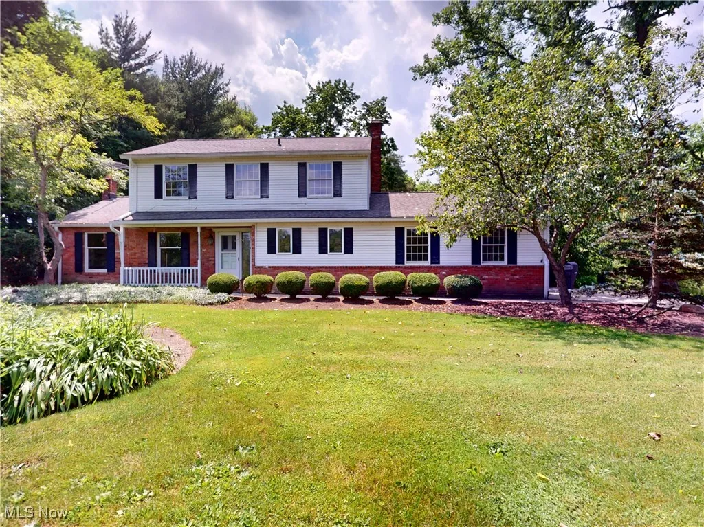 View of front facade with brick siding, a chimney, a front yard, and covered porch