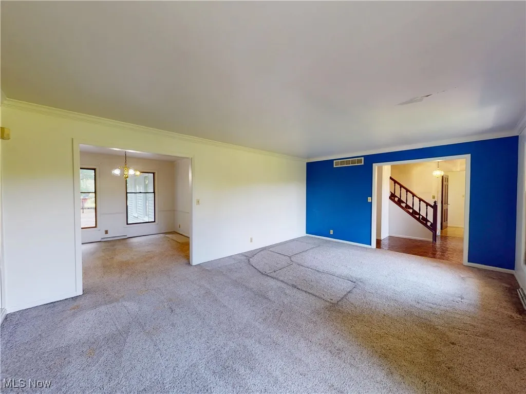 Carpeted spare room featuring a chandelier, crown molding, and stairway