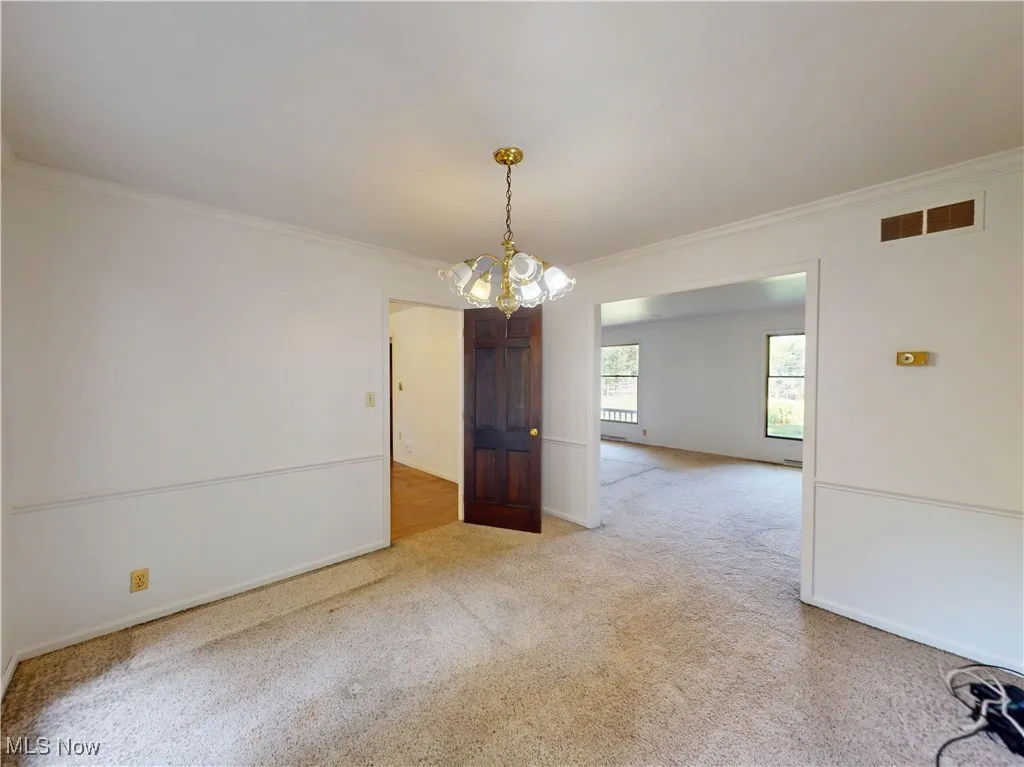 Carpeted empty room with crown molding and a chandelier