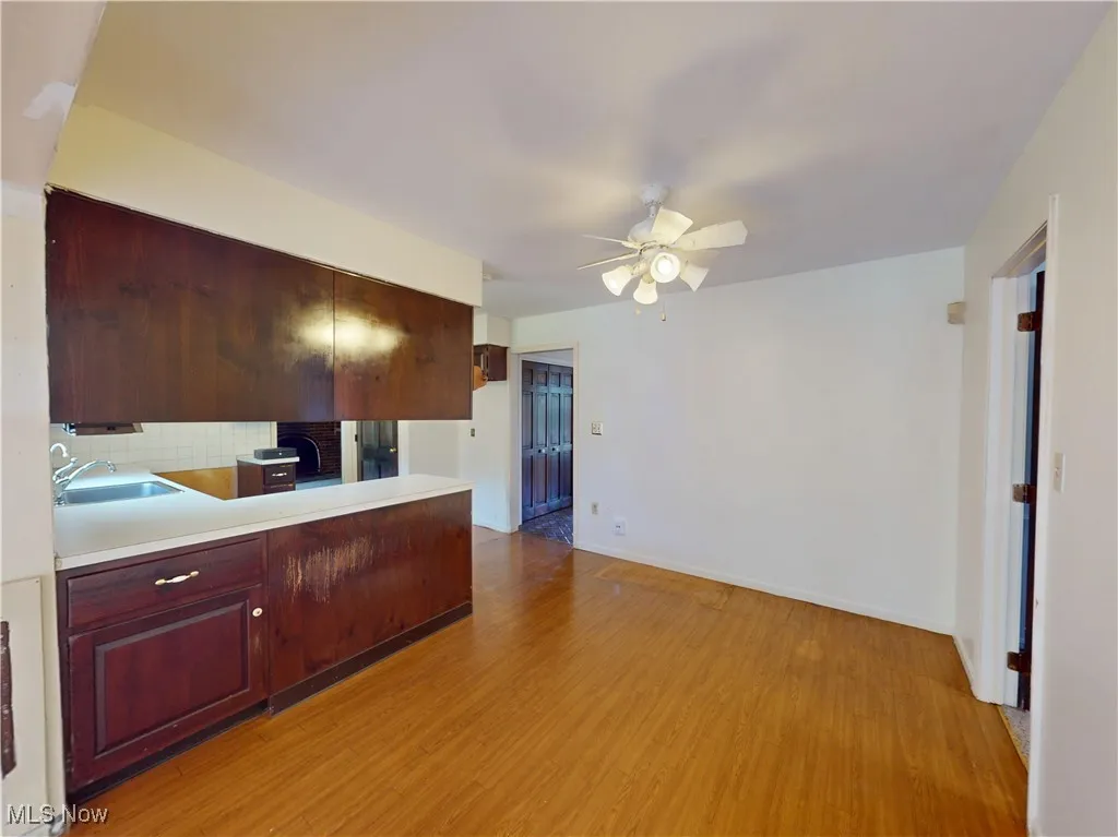 Kitchen with light wood-type flooring, tasteful backsplash, ceiling fan, light countertops, and dark brown cabinets