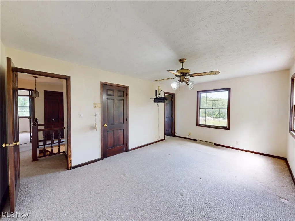Unfurnished bedroom featuring multiple windows, carpet floors, a textured ceiling, and a ceiling fan