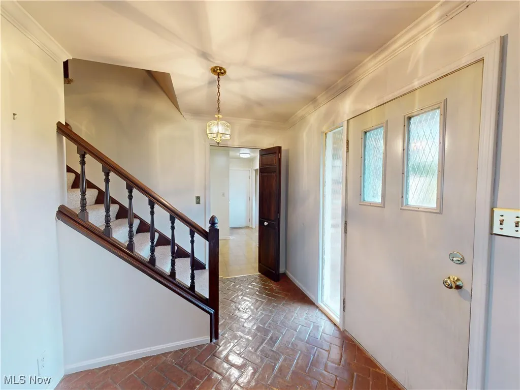 Entryway featuring brick flooring, crown molding, and stairway