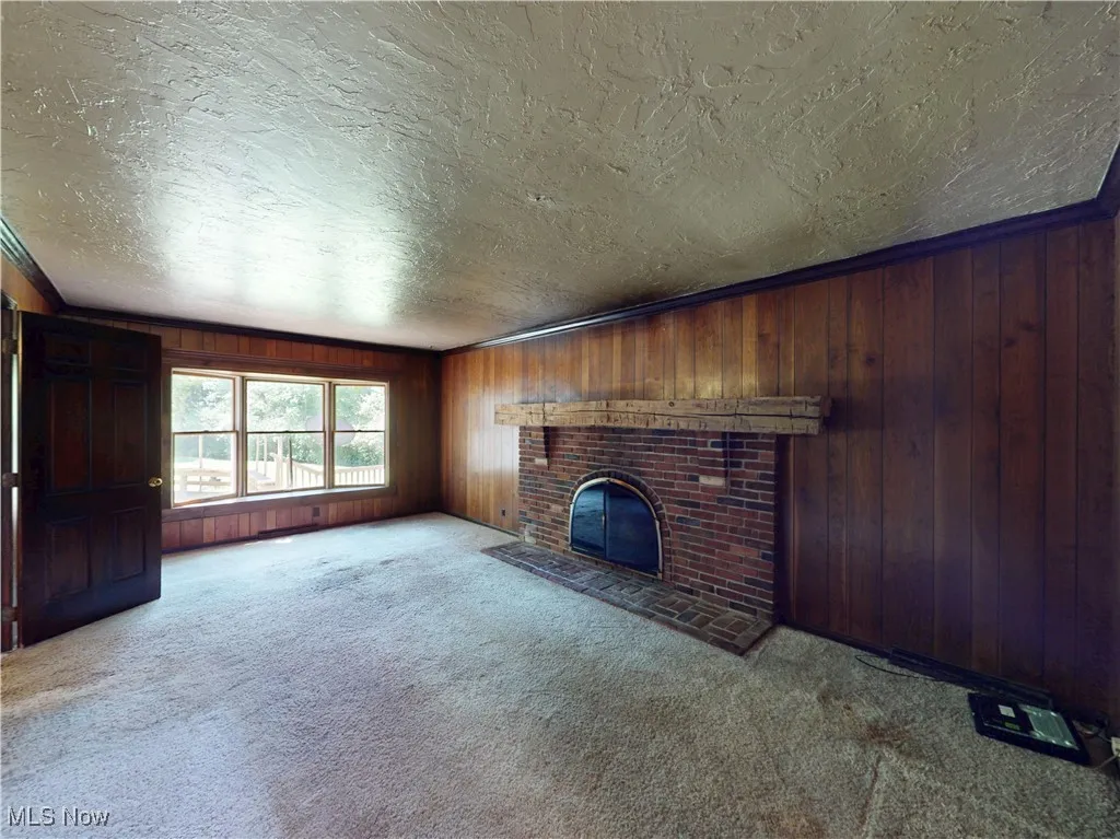 Unfurnished living room featuring a textured ceiling, carpet floors, a fireplace, and wood walls