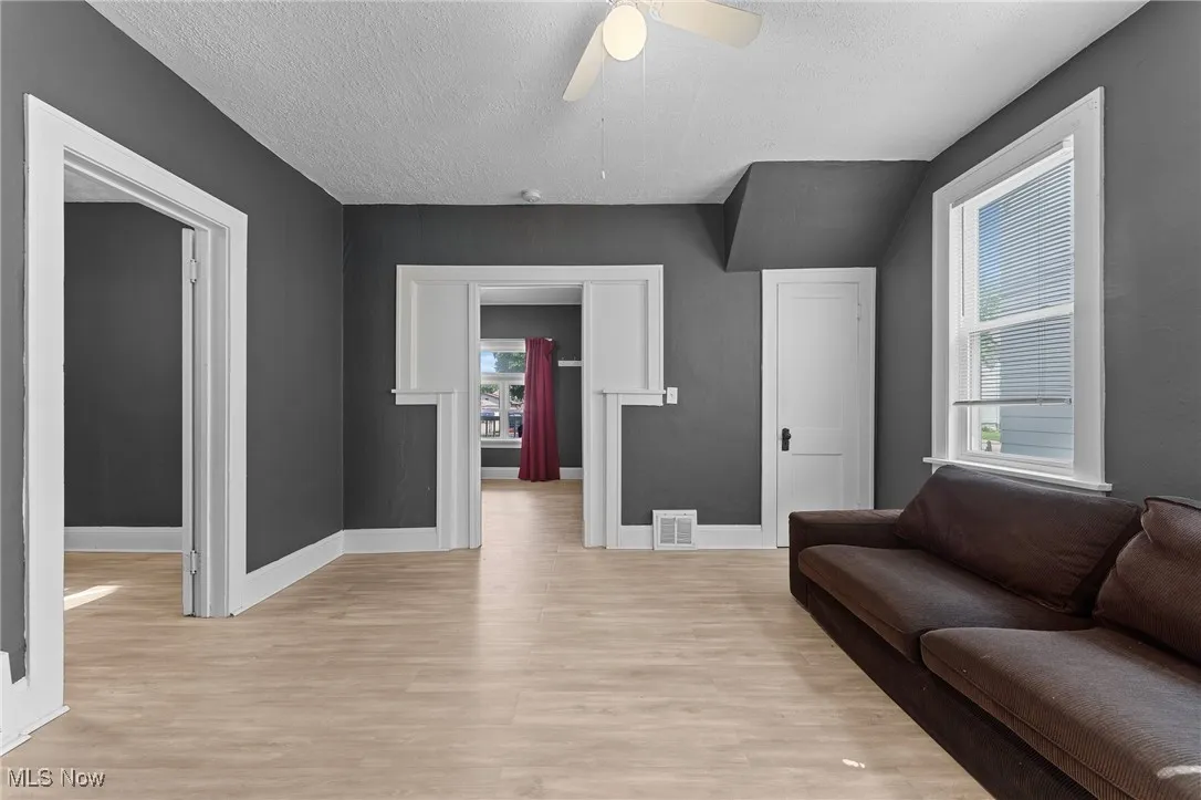 Living room with light wood-style floors, healthy amount of natural light, ceiling fan, and a textured ceiling