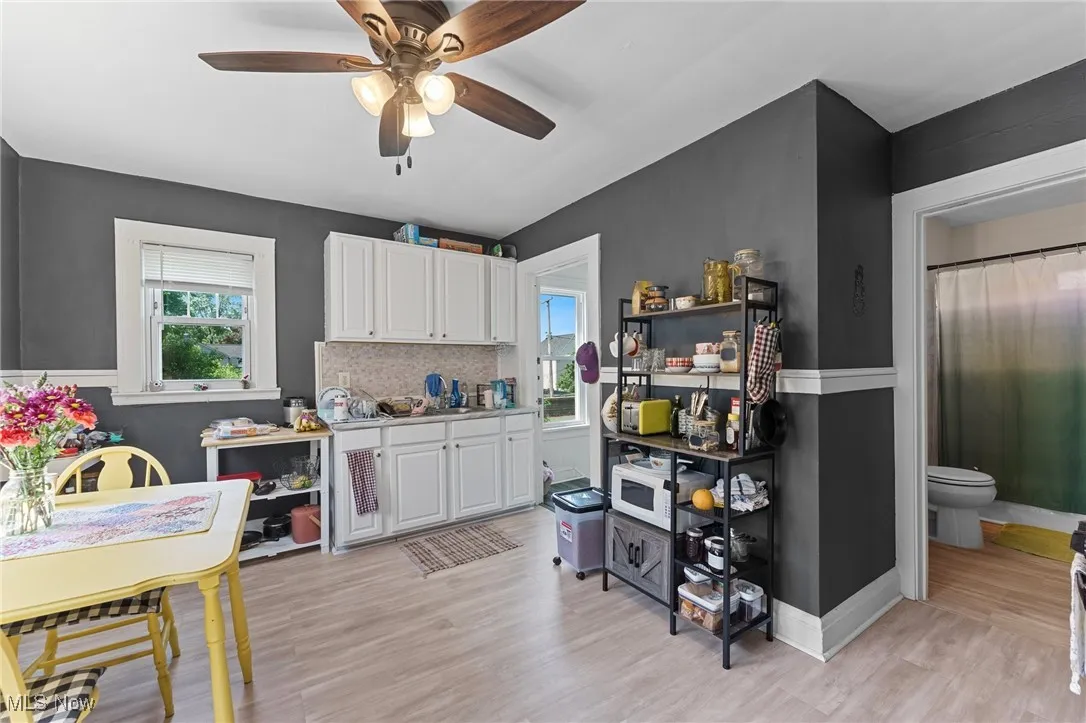 Kitchen with ceiling fan, white cabinets, light wood-type flooring, and light countertops