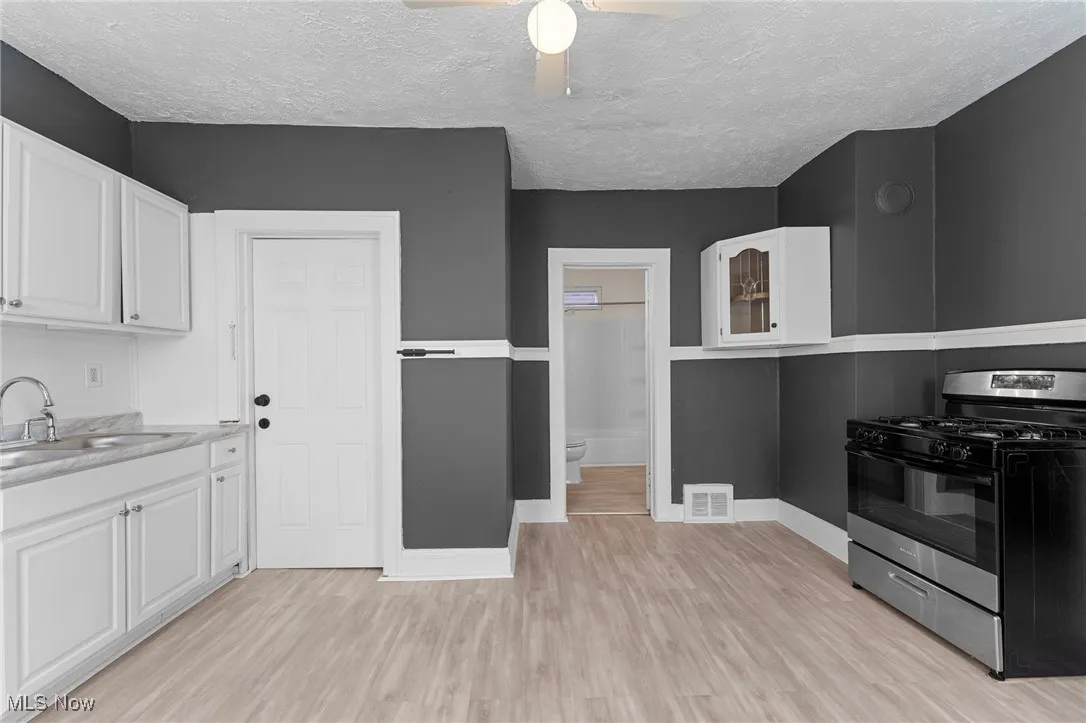 Kitchen featuring stainless steel range with gas cooktop, white cabinets, light wood finished floors, a ceiling fan, and a textured ceiling