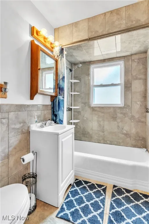 Full bathroom with shower / bath combination, vanity, and tile walls