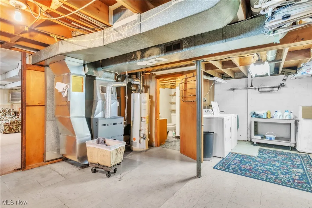 Unfinished below grade area featuring tile patterned floors, water heater, heating unit, and independent washer and dryer