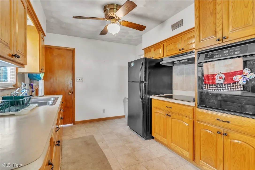 Kitchen featuring black appliances, under cabinet range hood, a ceiling fan, decorative backsplash, and brown cabinetry