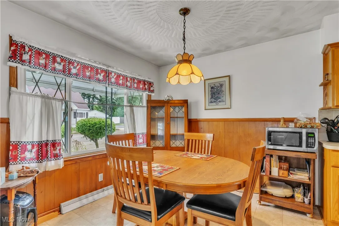 Dining space featuring a wainscoted wall, wooden walls, a baseboard radiator, and light tile patterned floors